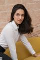 A woman in a white shirt and black pants posing on a yellow couch.