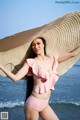 A woman in a pink bikini and a straw hat on the beach.