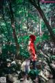 A woman in a red hooded outfit standing on a rock in the woods.