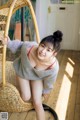 A woman sitting in a wicker chair on a wooden floor.