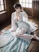 A woman in a blue and white dress sitting on a wooden floor.