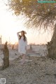 A woman in a white dress standing next to a tree.