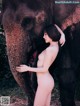 A naked woman standing next to an elephant.