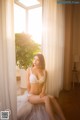 A woman in a white lingerie sitting on a window sill.