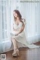 A woman in a white dress sitting on a window sill.