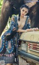 A woman leaning on the back of a car next to an elephant.