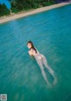 A naked woman floating in the clear blue water of a beach.