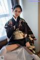 A woman in a black kimono sitting on a bed.