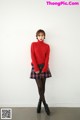 A woman in a red sweater and plaid skirt posing for a picture.