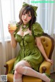 A woman in a green dress sitting on a yellow chair holding a glass of orange juice.