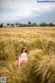 A woman in a pink dress sitting in a field of wheat.