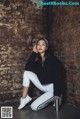 A woman sitting on the ground in front of a brick wall.