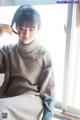 A woman sitting on a window sill wearing a gray sweater.